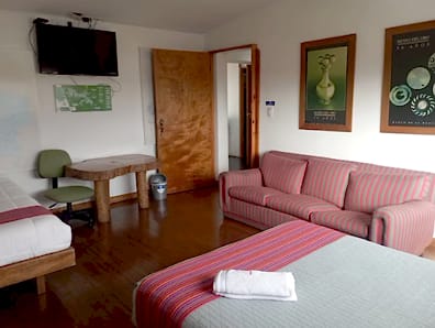 Habitación privada con dos camas de cobijas a rayas, sofá rosado, televisor, escritorio y piso de madera.